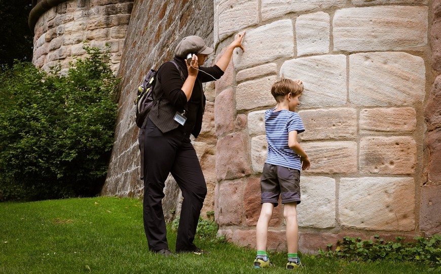 Kind steht mit der Rundgangsleiterin an der Nürnberger Stadtmauer und untersucht die Steine.