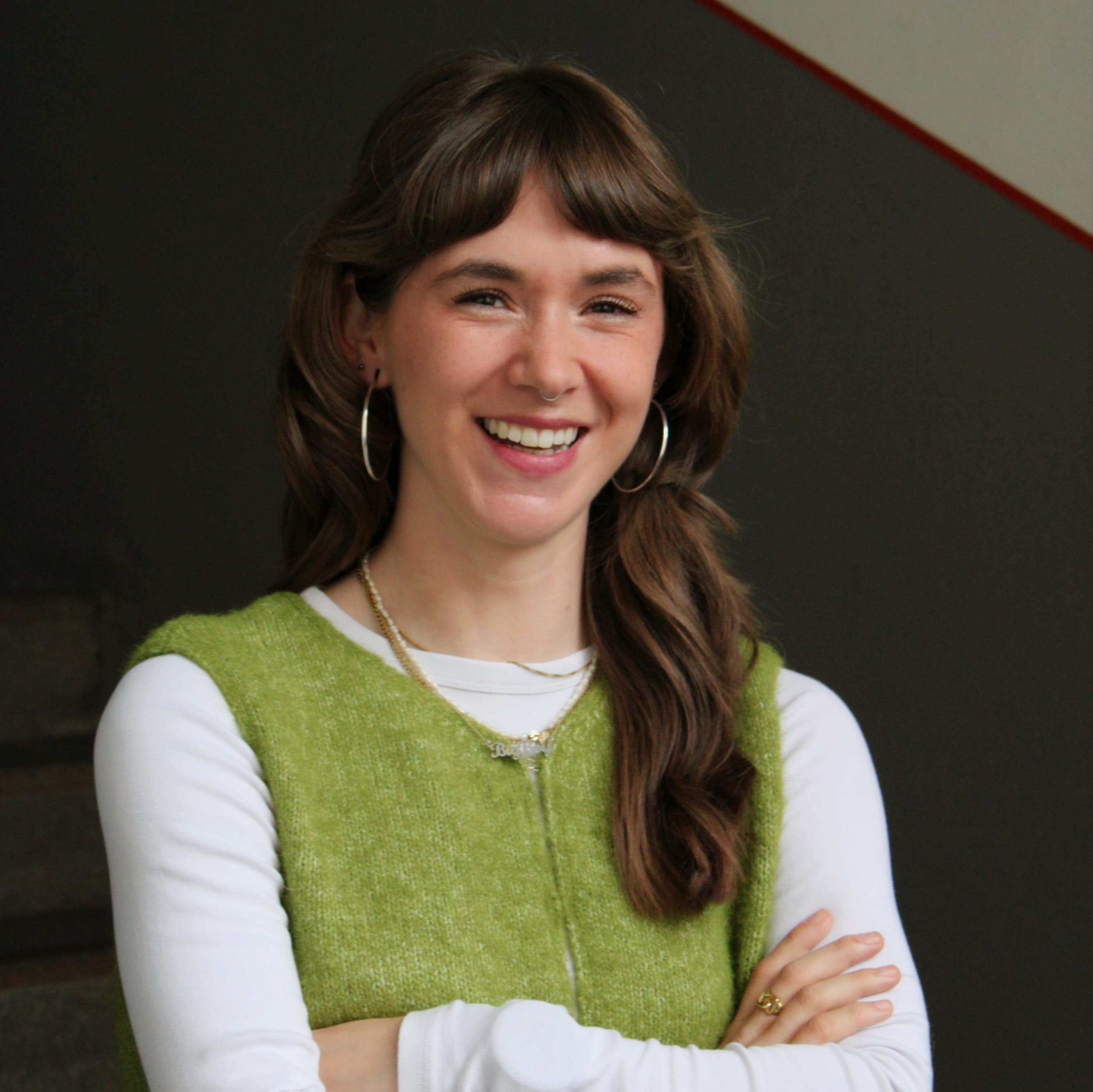 Emily MacKenzie arbeitet als Werkstudentin bei Geschichte Für Alle e.V.. Auf dem Bild trägt sie eine grüne Weste und lächelt in die Kamera.