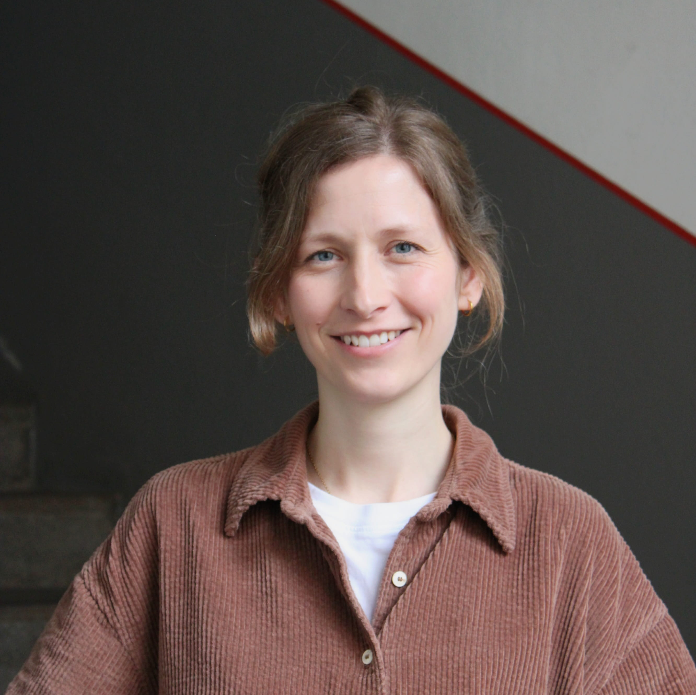 Jasmin Schmitt ist wissenschaftlich-pädagogische Mitarbeiterin bei Geschichte Für Alle e.V.. Auf dem Foto trägt sie ein braunes Hemd und blickt lächelnd in die Kamera.