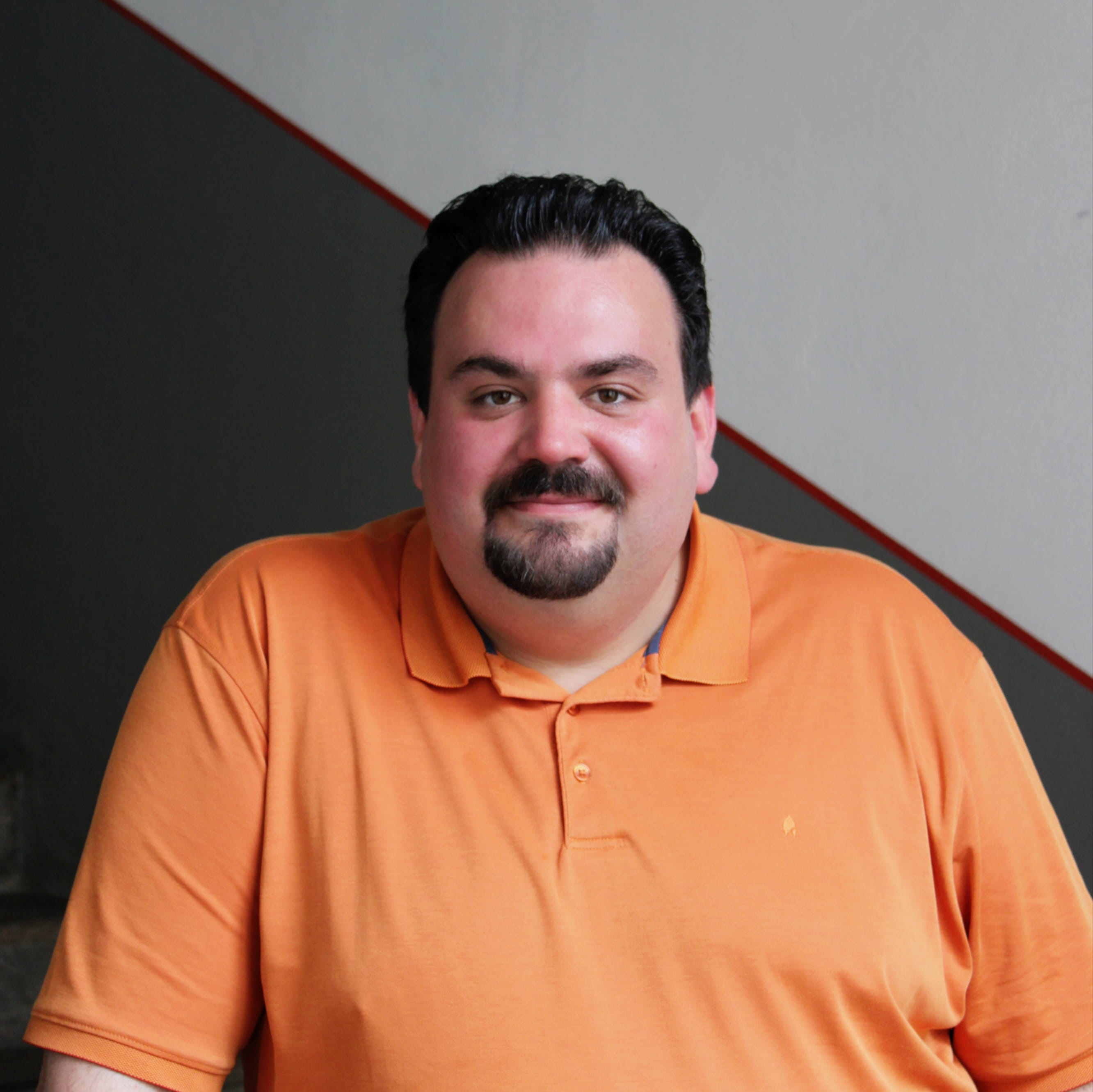 Stefan Spangler arbeitet im Bereich Schiffs- und Bustouren Nürnberg. Er trägt ein orangefarbenes Oberteil und blickt lächelnd in die Kamera.