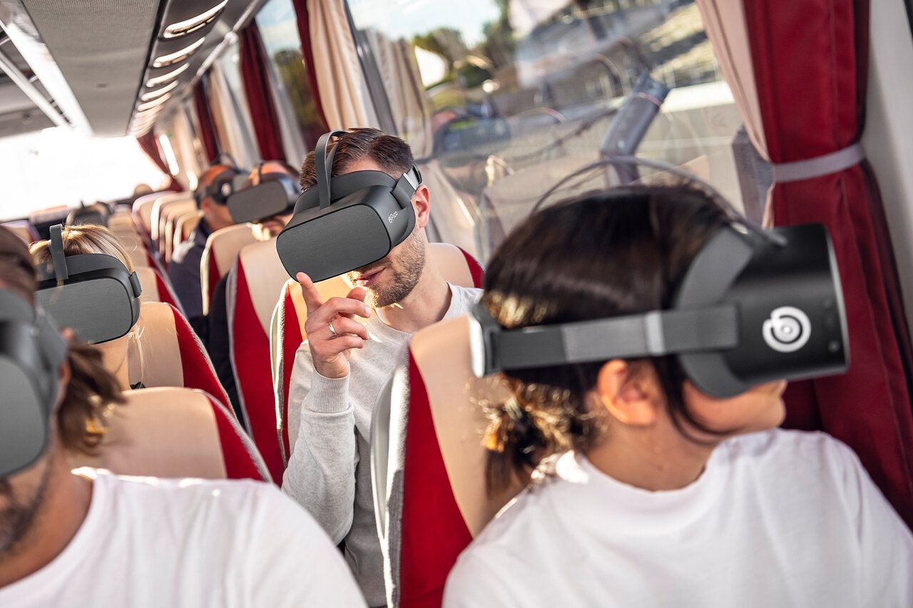 Gäste sitzen mit VR-Brillen in einem Bus und blicken aus dem Fenster
