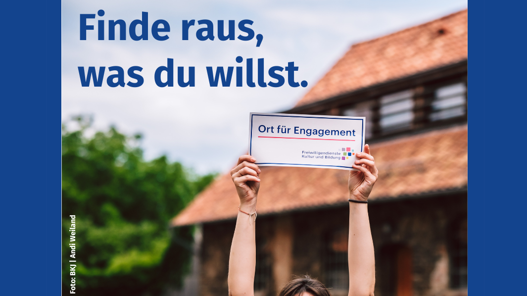 Fotografie mit einem unscharfem Gebäude im Hintergrund. Die Schrift "Finde raus, was du willst" ist über den Himmel im linken Bildrand gelegt. Im Vordergrund sind zwei Arme sichtbar die ein Schild hochhalten. Auf dem Schild steht "Ort für Engagement Freiwilligendienste Kultur und Bildung"." 