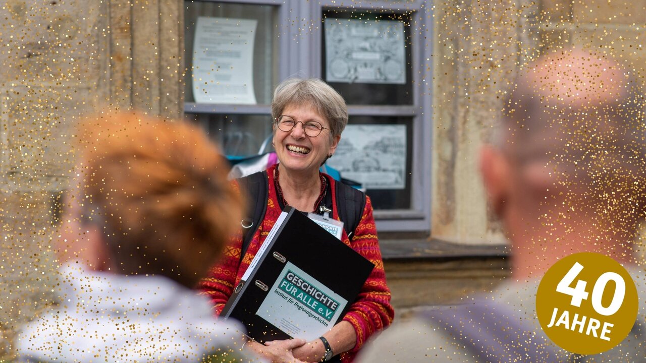 Stadtführerin Birgit Fecher lacht mit Gästen, die im unscharf im Vordergrund zu sehen sind, rechts ein goldener Kreis mit '40 Jahre', dazu goldenes Konfetti über das Bild verteilt