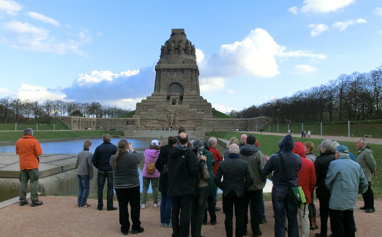 Eine Gruppe Menschen von hinten fotografiert, im Hintergrund das Völkerschlachdenkmal in Leipzig
