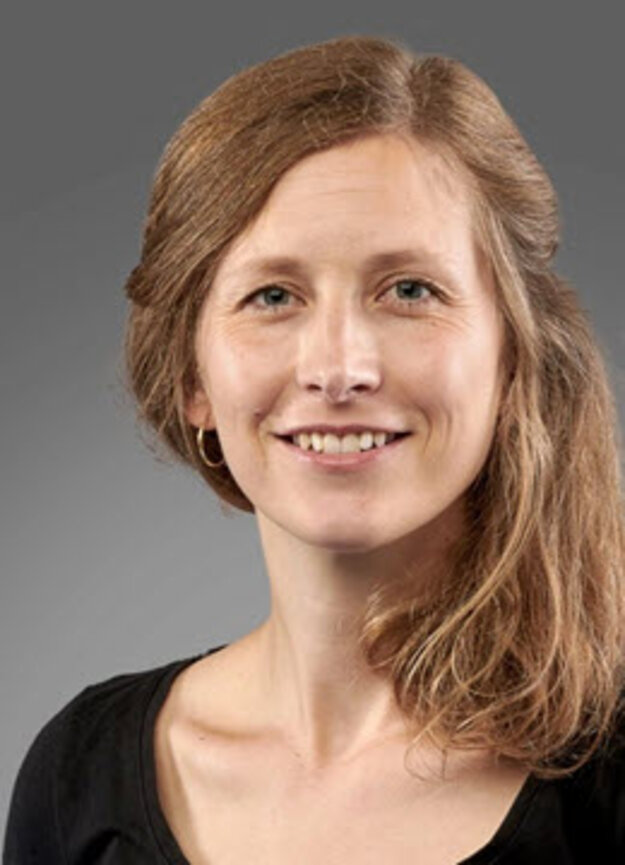 Mitarbeiterin Jasmin Schmitt, lächelnd vor grauem Hintergrund