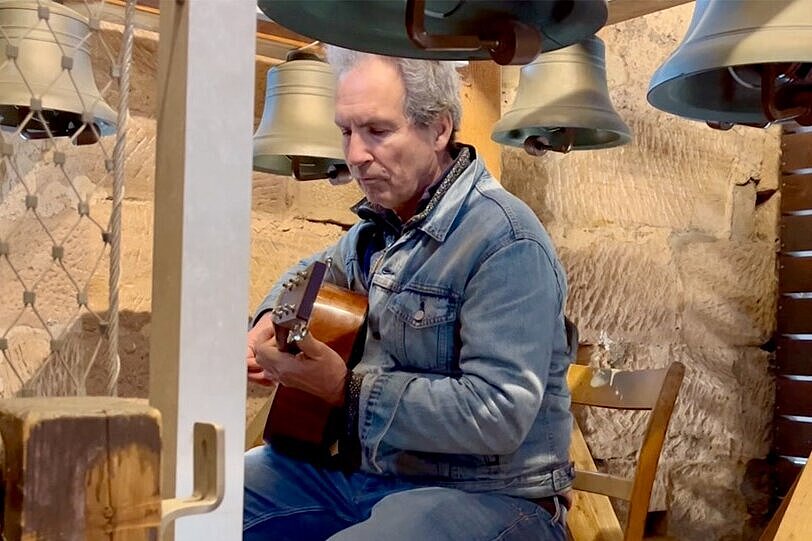 Rundgangsleiter Dr. Alexander Mayer begleitet das Glockenspiel im Fürther Rathaus auf seiner Gitarre. Alexander Mayer sitzt Gitarre spielend unter dem Glockenspiel des Fürther Rathauses