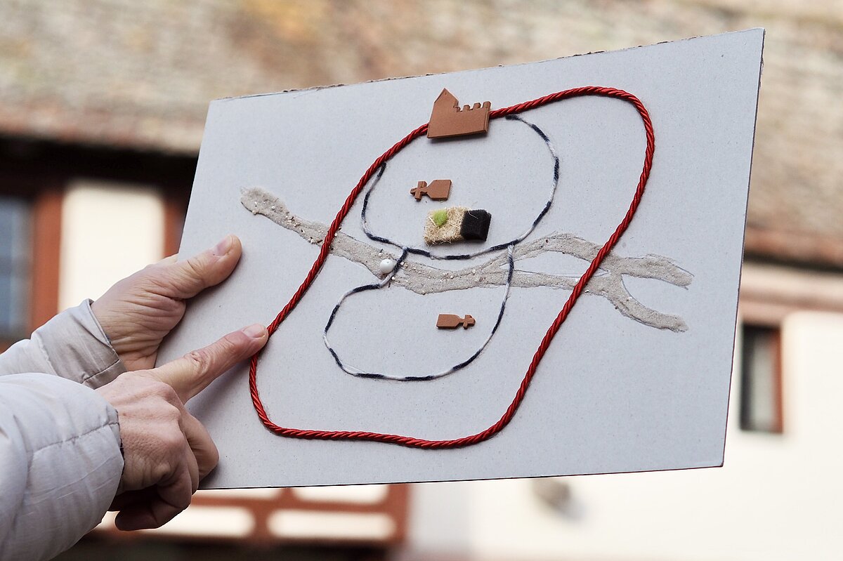 Ein Tastmodell der Nürnberger Altstadt wird von einer Hand senkrecht nach oben gehalten, während es die andere Hand abtastet, im Hintergrund ein Fachwerkhaus