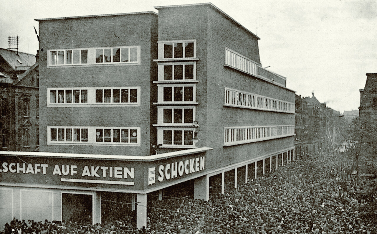 Schwarzweißaufnahme von einem großen Gebäude mit Aufschrift 'von Aktien', in den Straßen um das Gebäude eine große Menschenmenge