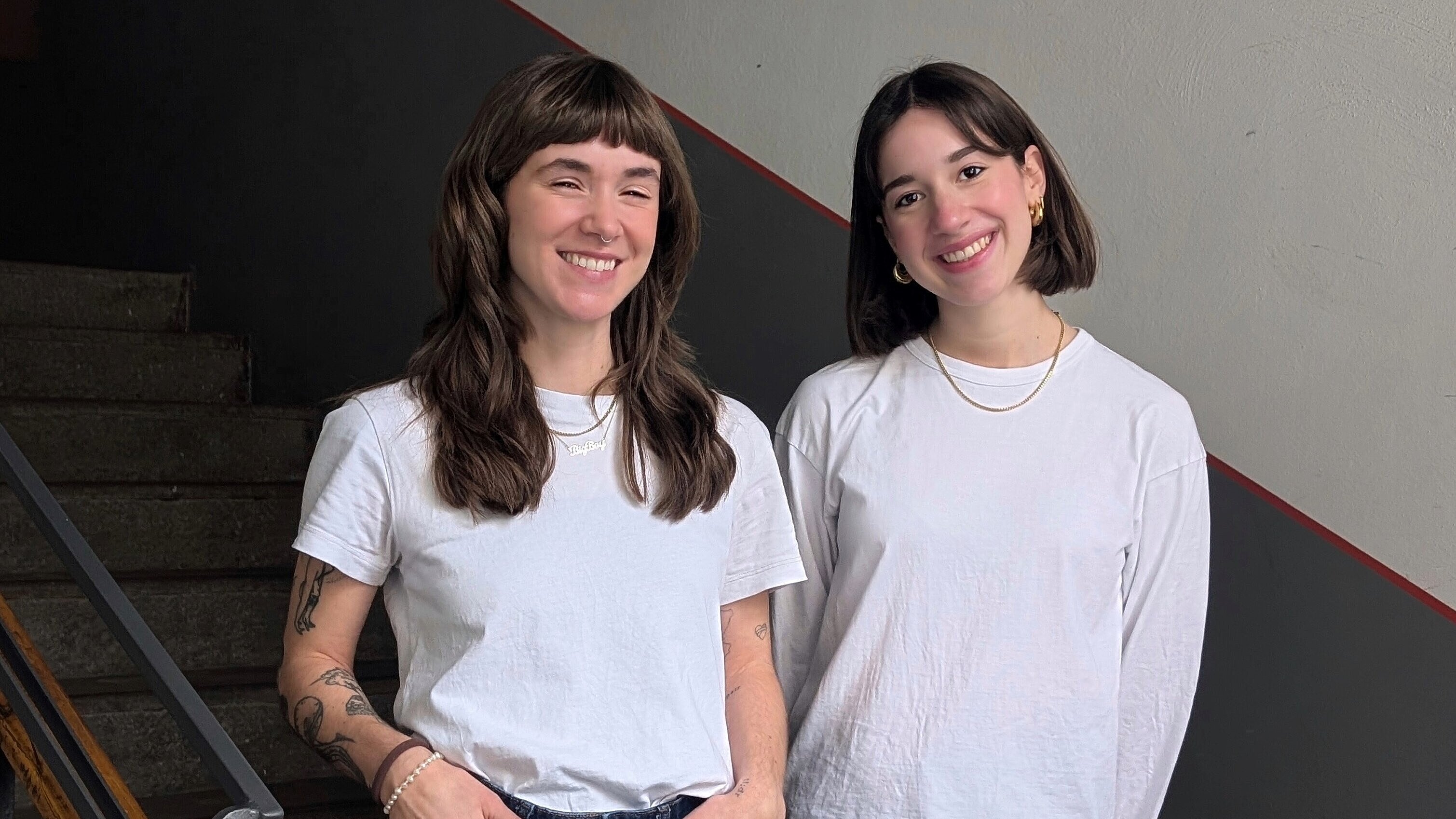 Zwei Frauen mit weißen T-Shirts stehen in einem Treppenhaus. 