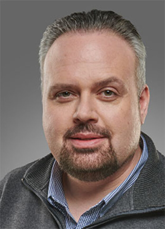 Mitarbeiter Pascal Metzger, lächelnd vor grauem Hintergrund