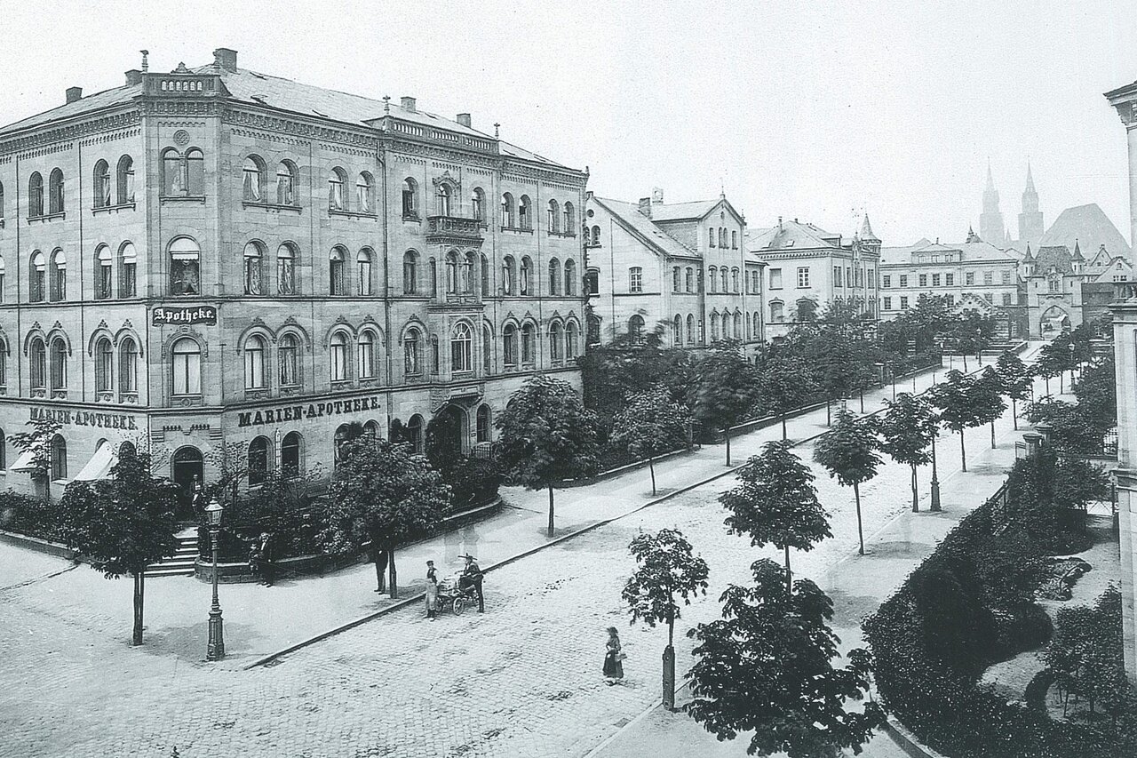 Schwarzweißaufnahme der Marienvorstadt, rechts ein großes Gebäude mit der Aufschrift 'Marienapotheke', rechts eine von Bäumen flankierte Straße