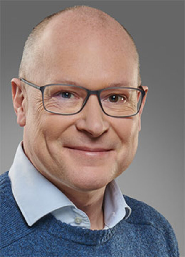 Freier Mitarbeiter Markus Urban, lächelnd vor grauem Hintergrund