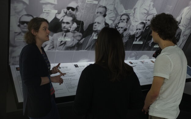 Ein Rundgang durch das Memorium Nürnberger Prozesse, links erklärt die Rundgangsleiterin, zwei Gäste sind von hinten zu sehen, im Hintergrund eine Ausstellungstafel
