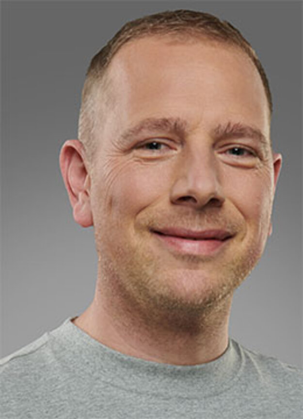 Freier Mitarbeiter Daniel Gürtler, lächelnd vor grauem Hintergrund