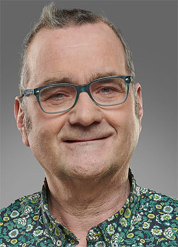 Freier Mitarbeiter Hartmut Heisig, lächelnd vor grauem Hintergrund