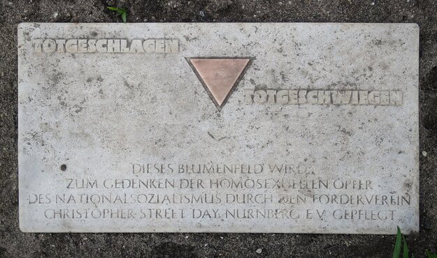Steintafel am Magnus-Hirschfeld-Platz in Nürnberg mit der Aufschrift "Totgeschlagen, totgeschwiegen. Dieses Blumenfeld wird zum Gedenken der homosexuellen Opfer des Nationalsozialismus durch den Förderverein Christopher Street Day, Nürnberg e.V. gepflegt
