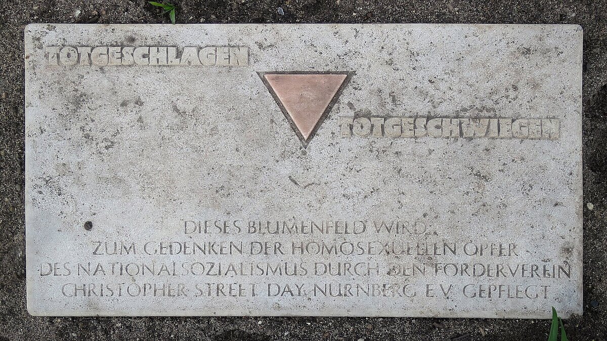 Steintafel am Magnus-Hirschfeld-Platz in Nürnberg mit der Aufschrift "Totgeschlagen, totgeschwiegen. Dieses Blumenfeld wird zum Gedenken der homosexuellen Opfer des Nationalsozialismus durch den Förderverein Christopher Street Day, Nürnberg e.V. gepflegt