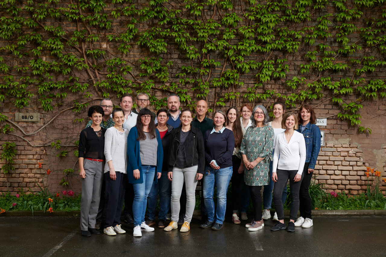 Gruppenfoto der Mitarbeiterinnen und Mitarbeiter vor einer mit wildem Wein bewachsenen Backsteinmauer
