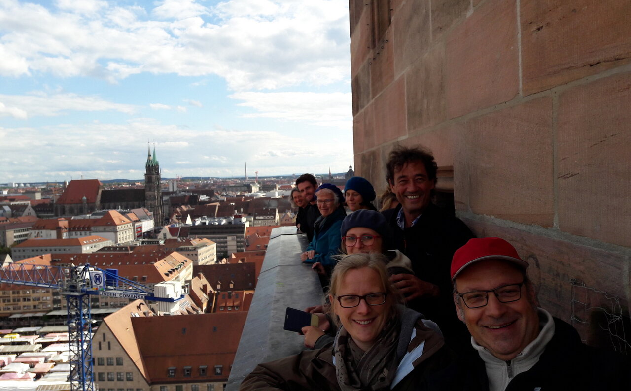 eine Gruppe Menschen auf dem Balkon eines Kirchturms am rechten Bildrand, links der Blick auf die Dächer der Nürnberger Altstadt