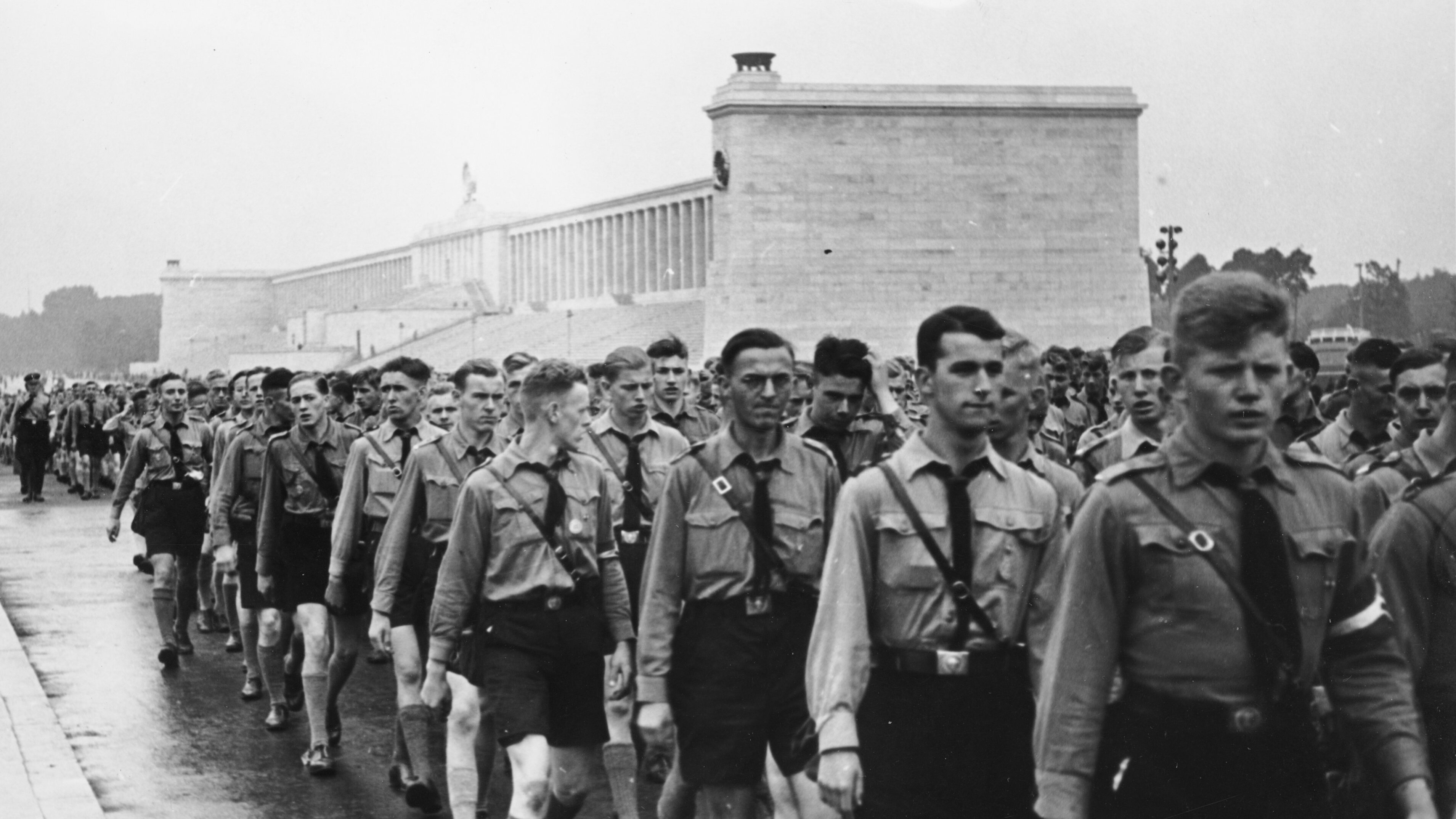 Im Hintergrund die Zeppelintribüne, im Vordergrund viele Männer der Hitlerjugend. Die jungen Männer tragen die gleiche Kleidung: langärmlige Hemden und kurze dunkle Hosen. 