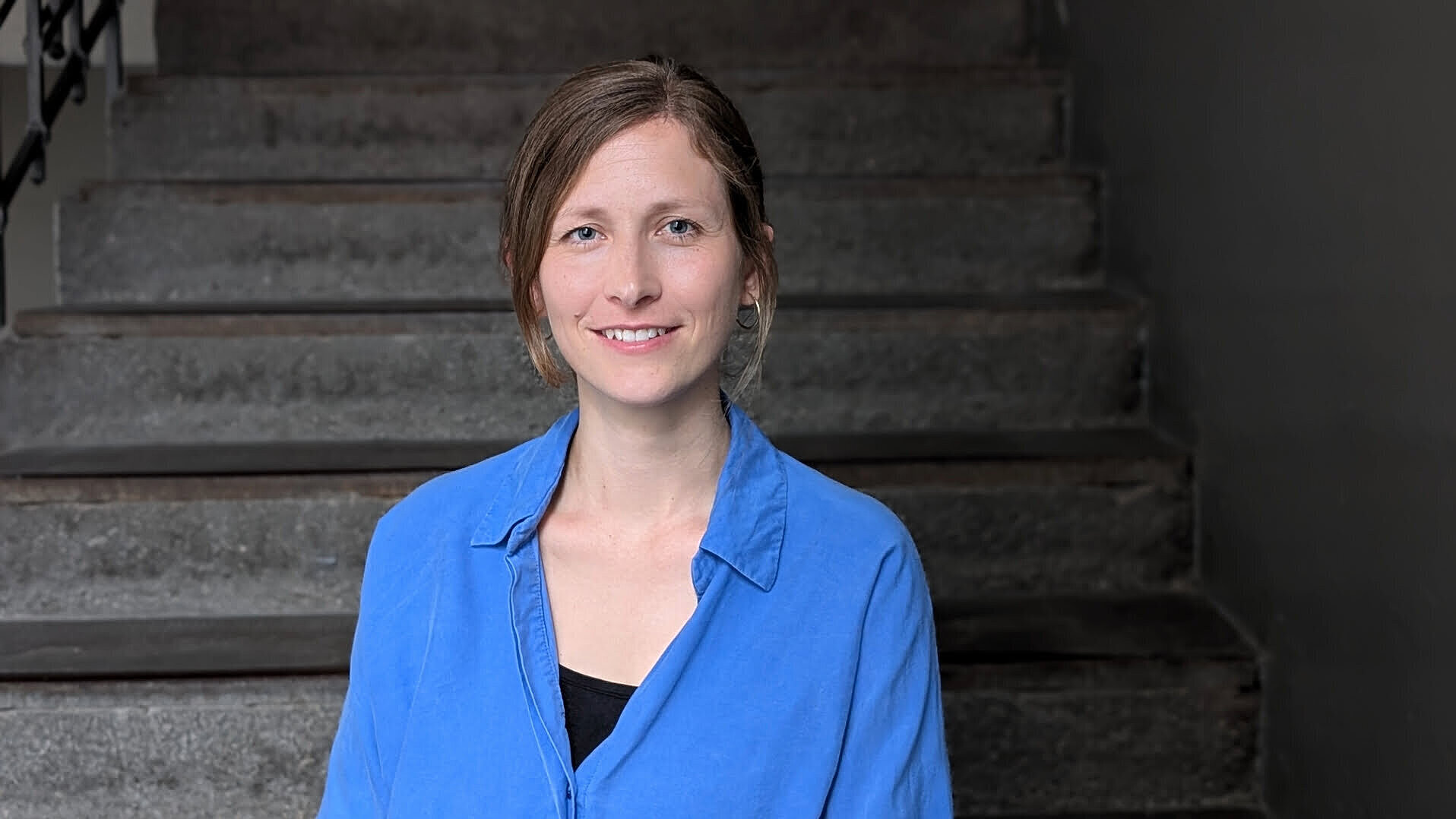 Mitarbeiterin Jasmin Schmitt lächelnd vor grauem Hintergrund