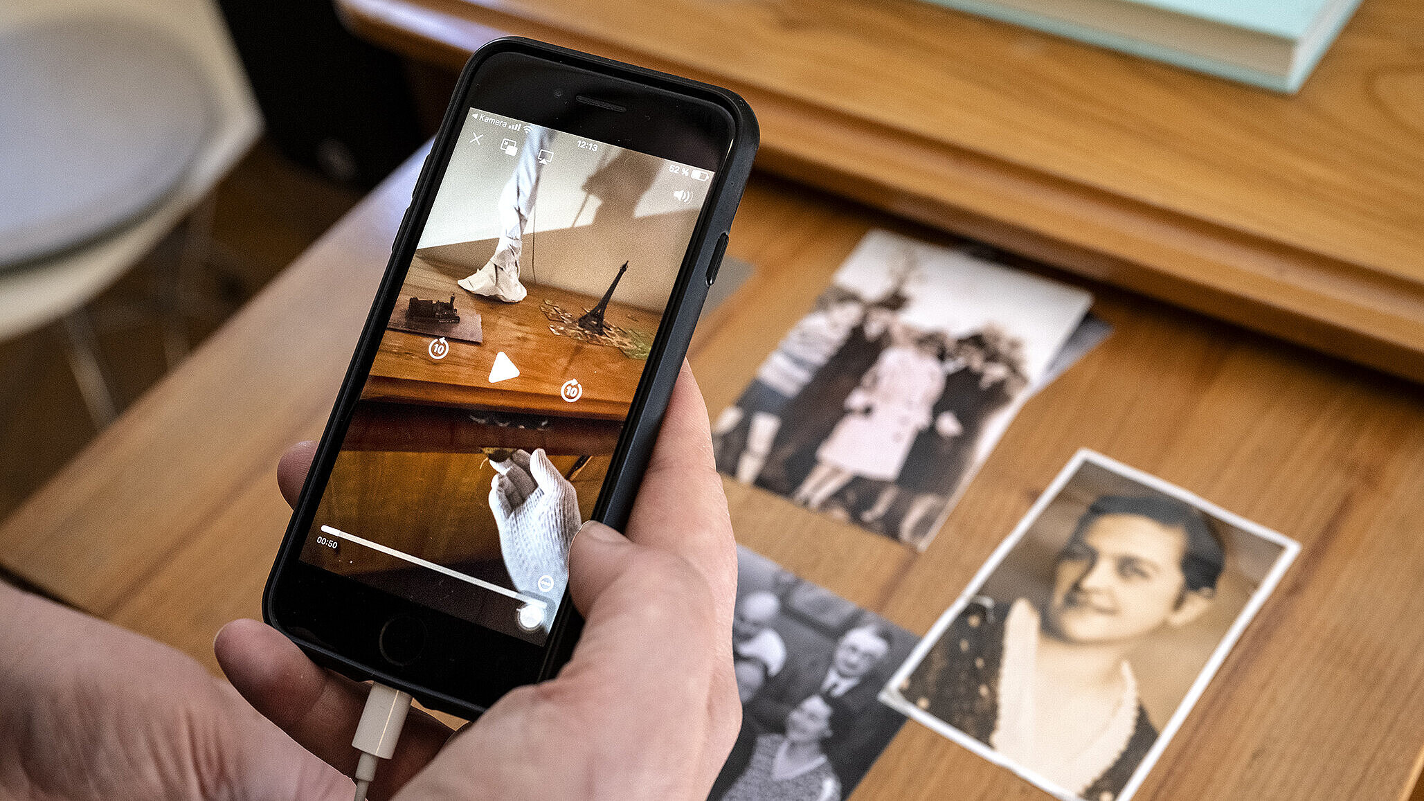 Eine Hand hält ein Smartphone, das eine Videosequenz zeigt, im Hintergrund eine Vitrine mit historischen Fotgrafien