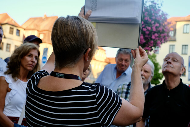 City guide photographed from behind holding up a folder with pictures, in the background guests listening out of focus