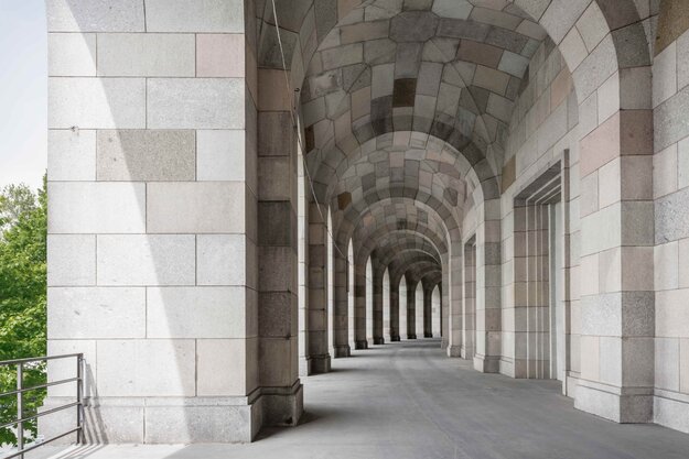 Fotografie mit Blick in den langen Säulengang der Kongresshalle in Nürnberg. In der Flucht sind die mit Granit verkleideten Säulen auf der linken Bildseite zu erkennen. Auf der rechten Bildseite verläuft eine Wand mit zugemauerten großen Toren in Granit.