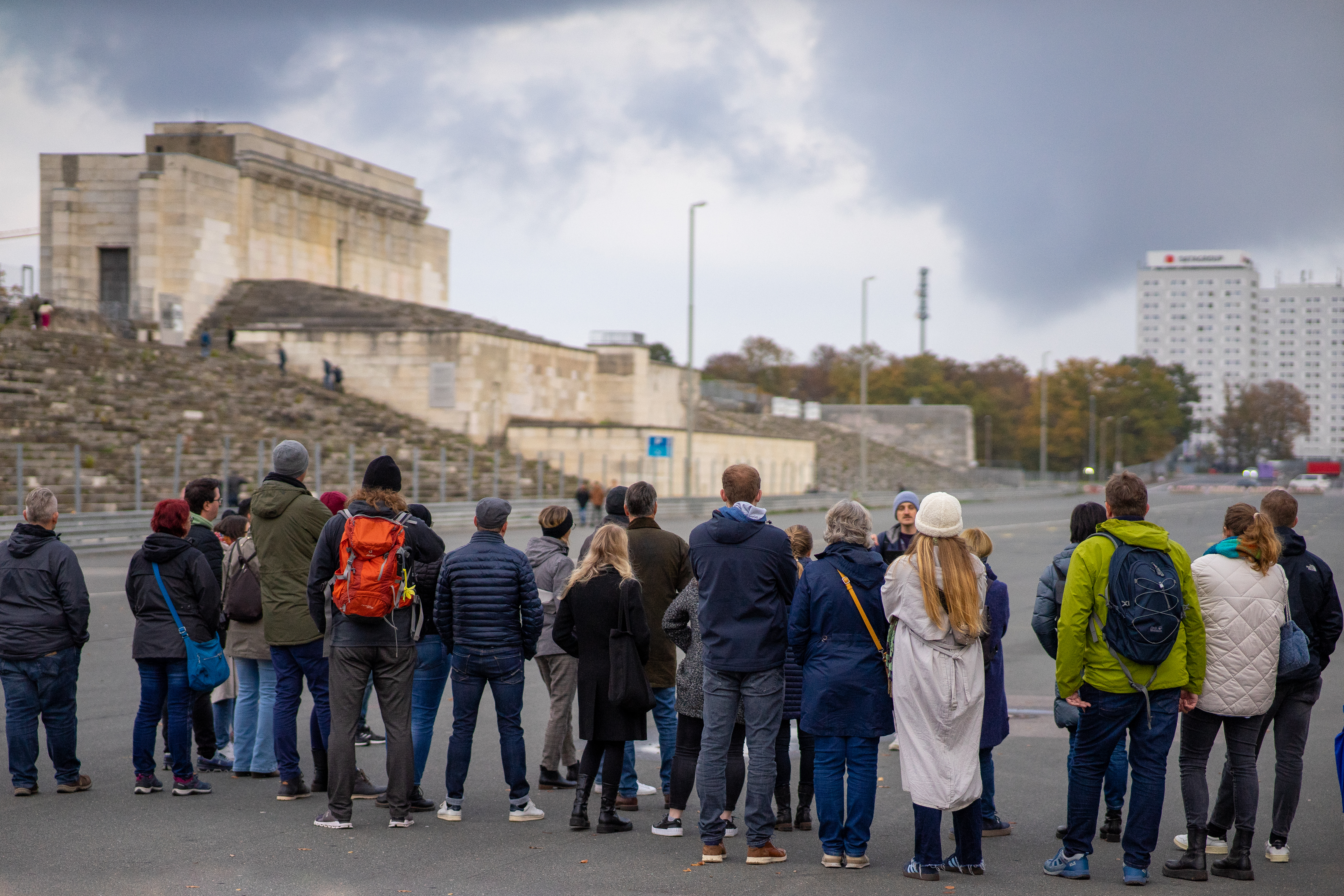 Eine Gruppe Menschen von hinten Fotografiert, im Hintergrund unscharf die Zeppelintribüne auf dem ehemaligen Reichsparteitagsgelände
