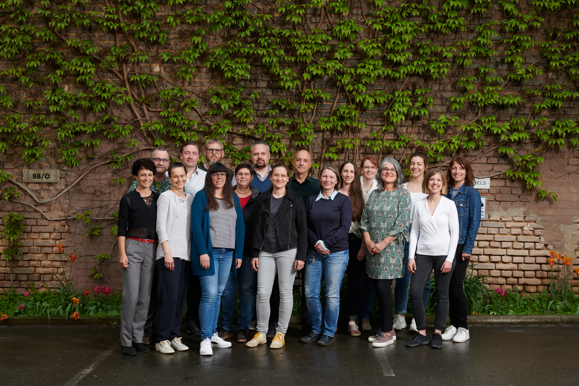 Gruppenfoto der Mitarbeiterinnen und Mitarbeiter vor einer mit wildem Wein bewachsenen Backsteinmauer